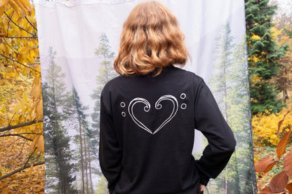 Person wearing a black long-sleeve shirt with a clef heart design in an autumn forest setting