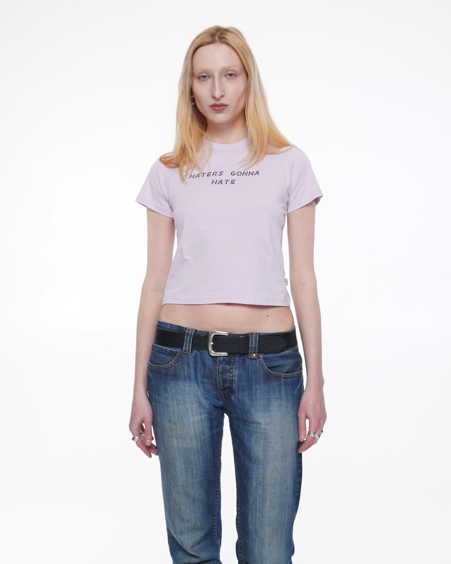 Person wearing a Light pink stretchy cotton baby T-shirt with a fitted silhouette and black rhinestone text "haters gonna hate"