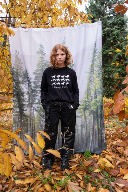 Person standing in front of a forest-themed blanket with autumn leaves around. Wearing black 100% cotton long sleeve shirt with silver silkscreen prints on the front, sleeves, and back.