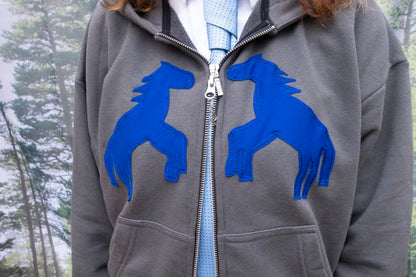 Gray hoodie with blue horse designs on a blurred natural background