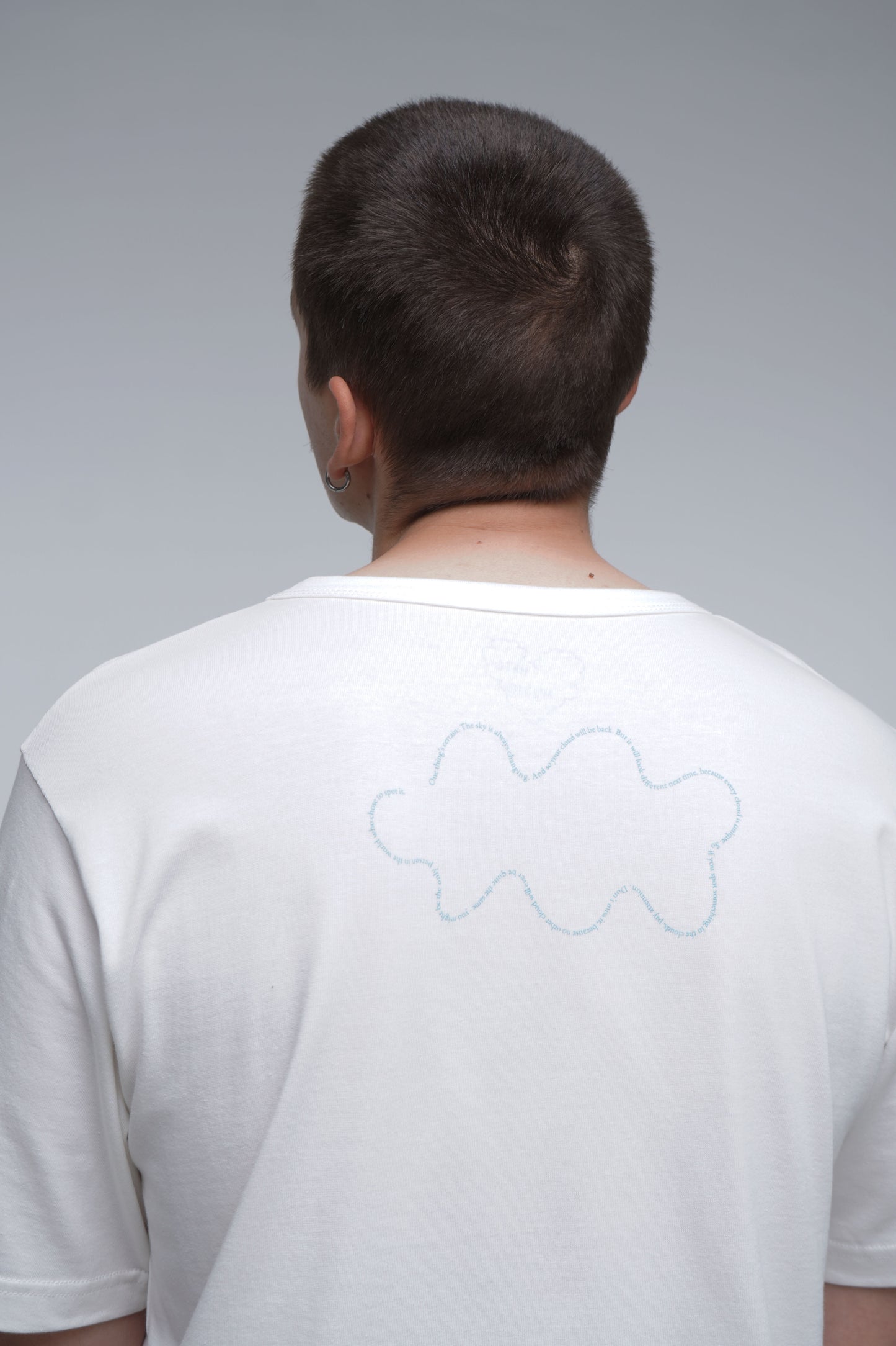 Person wearing a white t-shirt with a cloud design on the back against a gray background
