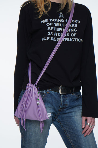 Person wearing a black sweatshirt with text, blue jeans, and carrying a purple mini bag crafted from durable raincoat fabric, designed for daily wear and personal styling with optional trinkets.